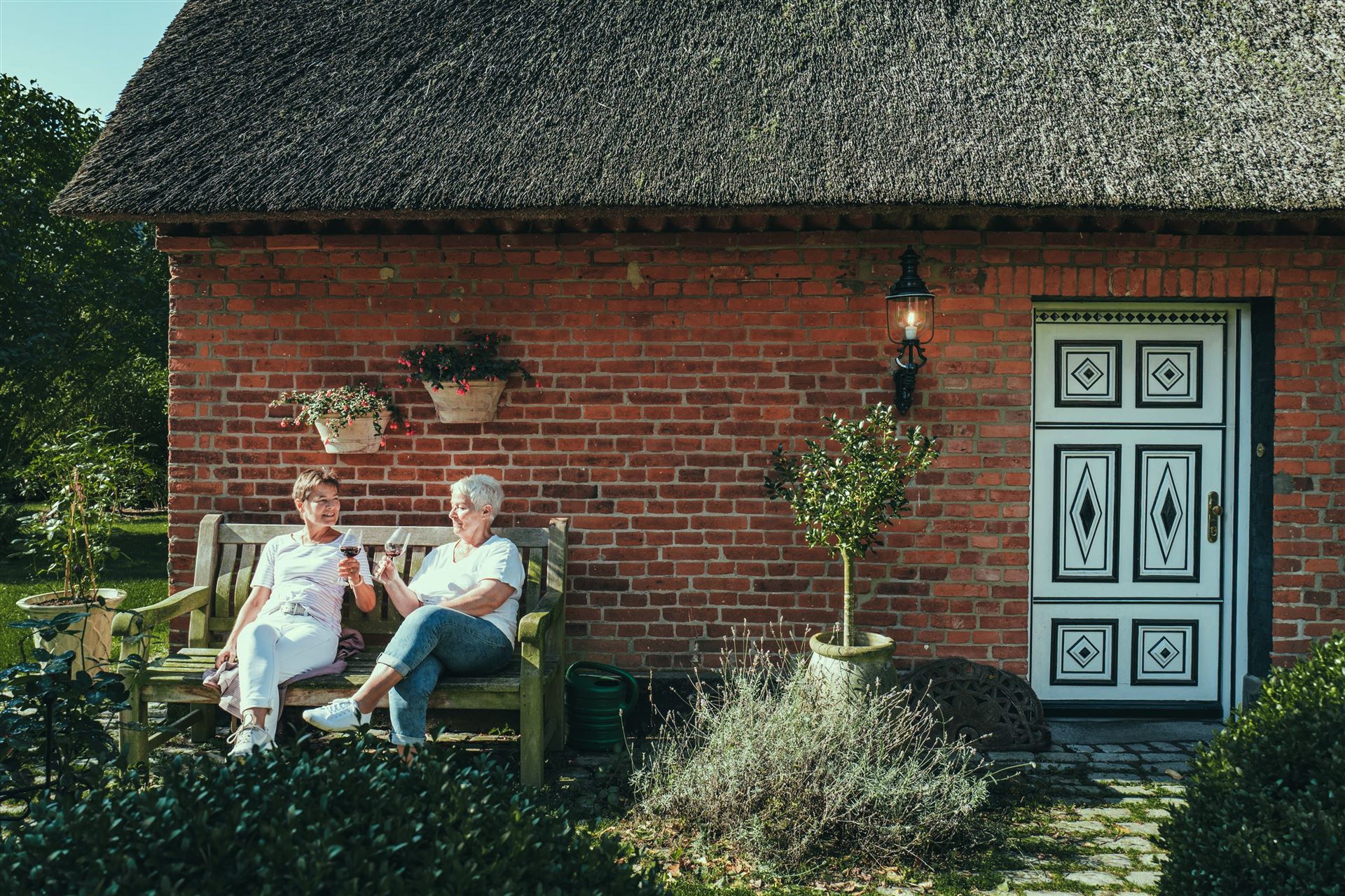 Zwei Frauen mit einem Weinglas vor einem Reetdachhaus in Grömitz.