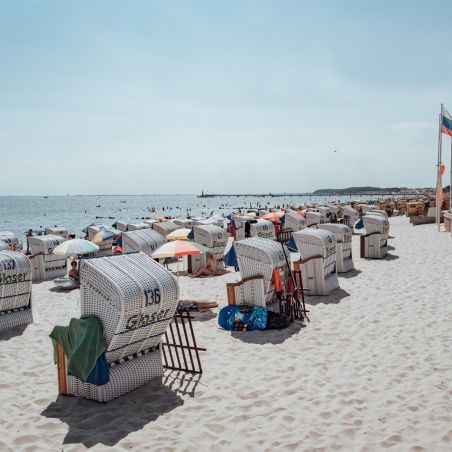 Strand mit zahlreichen Strandkörben, Menschen am Wasser und Flaggen im Hintergrund