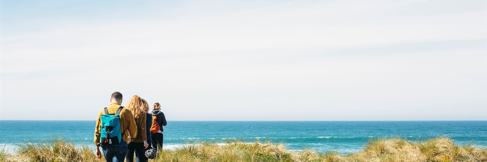 Drei Personen laufen auf einem schmalen Pfad durch Dünen zum Meer