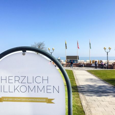 Willkommensschild an der Grömitzer Kurpromenade mit Blick auf Strand, Promenade und Meer im Hintergrund