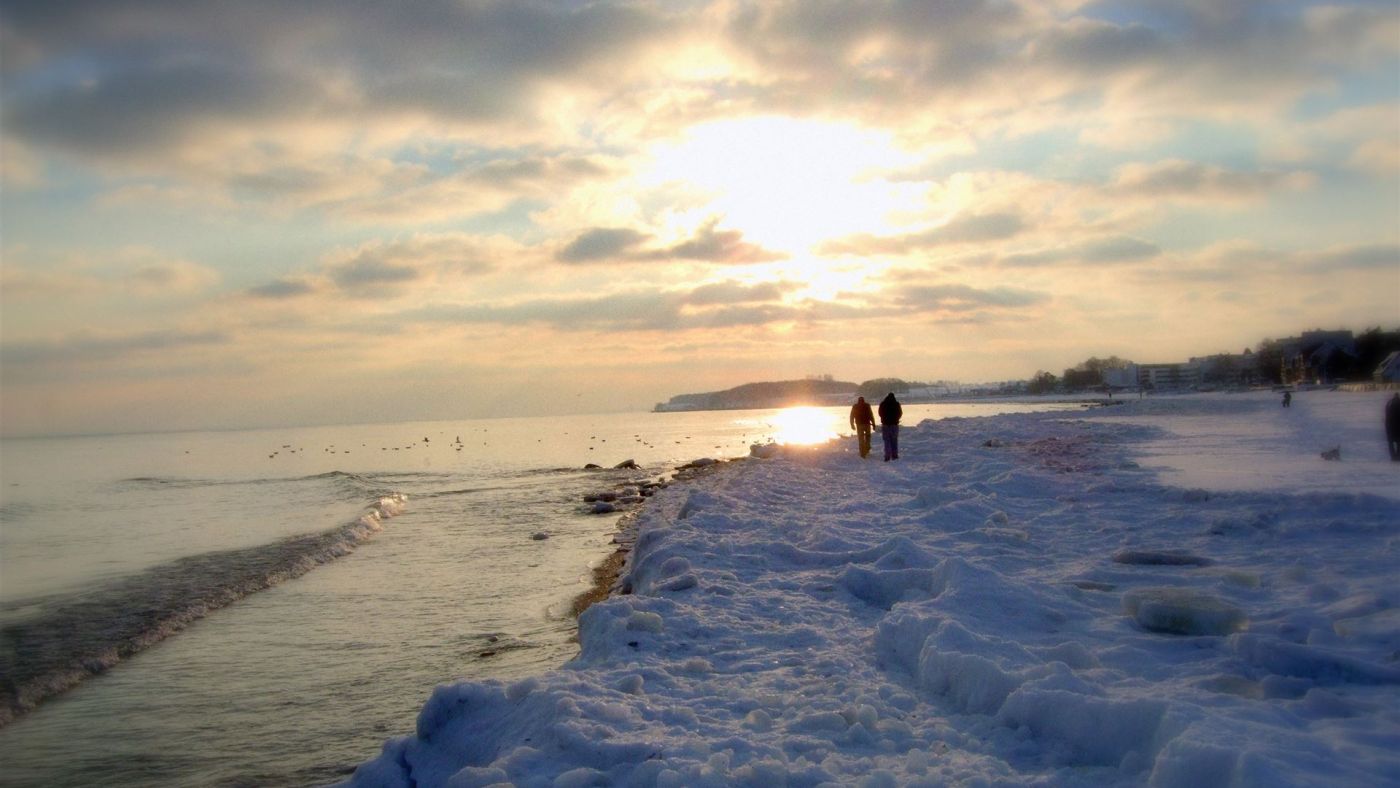Zwei Personen gehen an einem verschneiten Strand bei Sonnenuntergang entlang