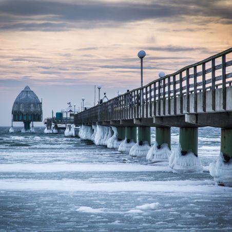 Eine Seebrücke mit vereisten Pfeilern im Winter bei Sonnenuntergang