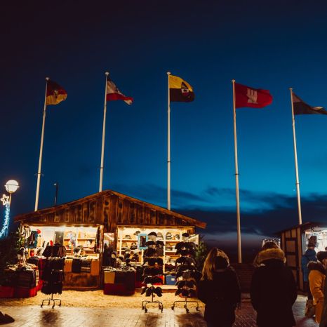 Weihnachtsmarktstände bei Nacht mit fünf wehenden Fahnen und Besuchern in Winterkleidung