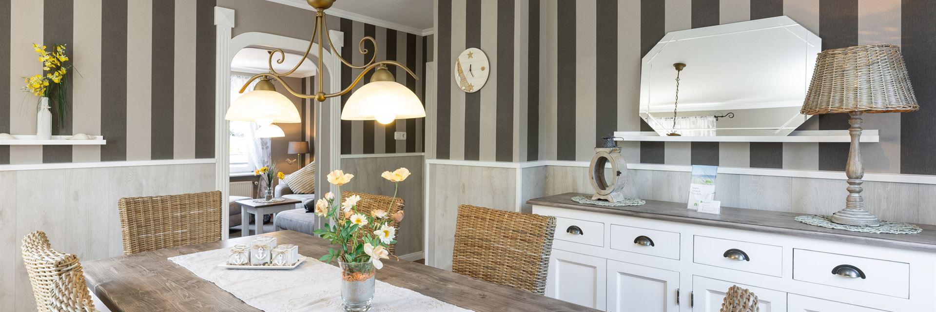 Überblick Esszimmer mit braun-taupe gestreiften Wändern, weiße Kommode im Apothekerstil und einem Esstisch für 6 Personen mit geflochteten Stühlen