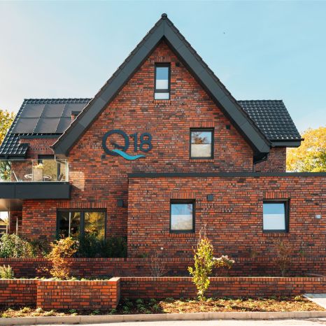 Modernes zweistöckiges Haus mit rotem Ziegelmauerwerk und schwarzem Dach mit Solarpanelen an sonnigem Tag