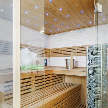 Innenraum einer modernen Sauna mit Holzbänken, beleuchtetem Holzdecke und Saunaofen mit Steinen