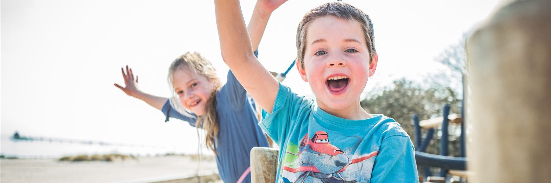 Zwei lachende Kinder, die auf einer Strandpromenade winken und Spaß haben.